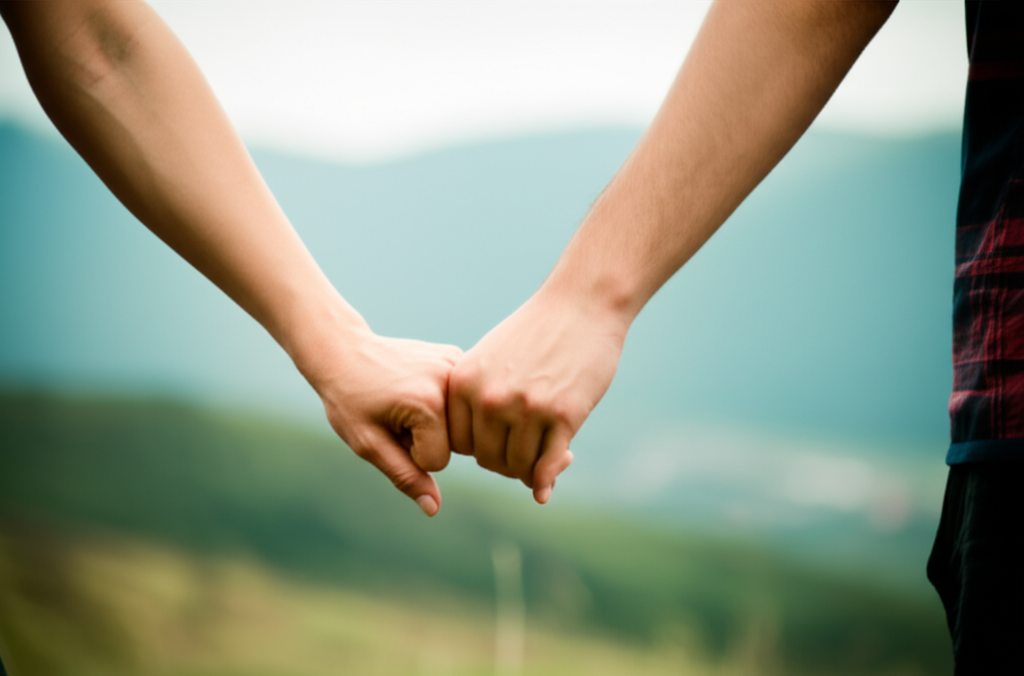 A close-up of two pairs of hands, one pair gently holding the other, with a blurred background of a serene natural landscape.