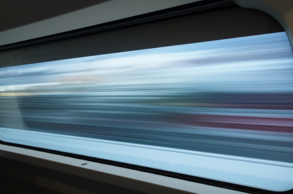 A blurry, motion-streaked landscape viewed from inside a transparent Hyperloop pod, showing only a sliver of the pod's interior and mostly the fast-moving scenery outside.
